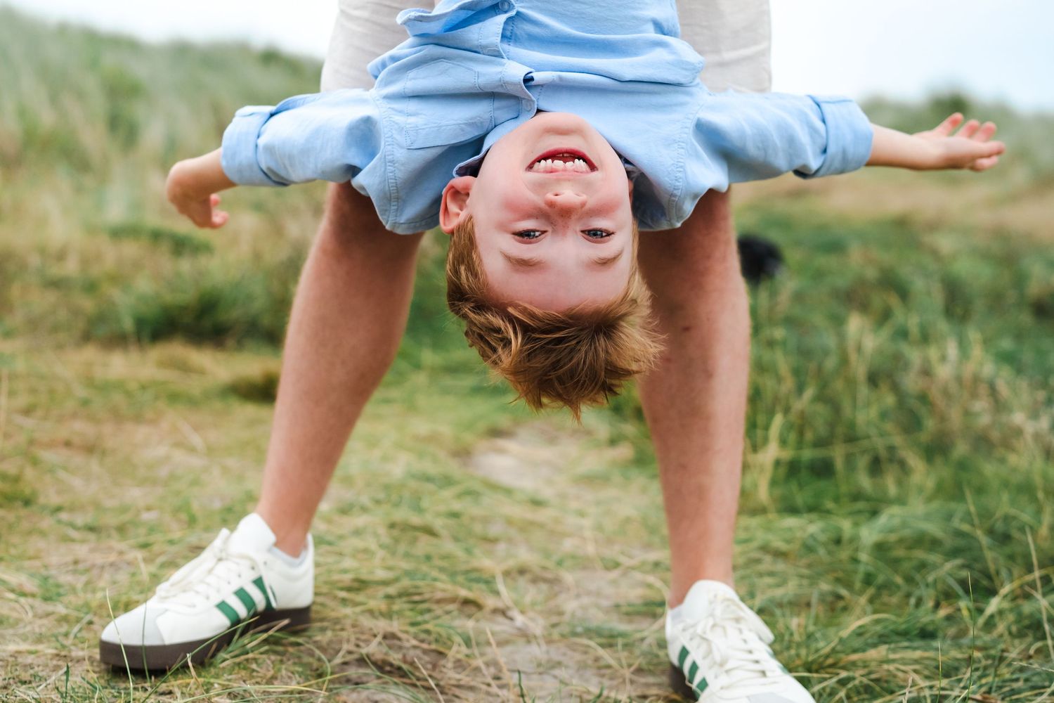 Children playing and laughing together in a grassy outdoor field on a sunny summer day.  Family photographer Dublin Ireland