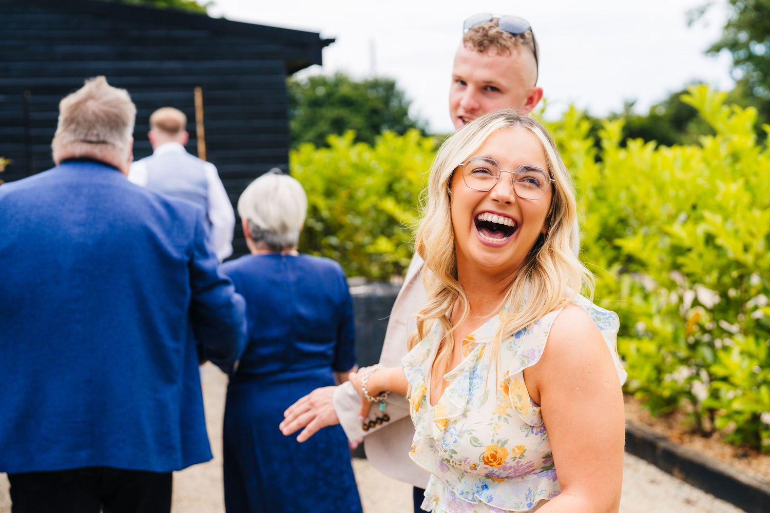 Poulaphouca Wedding photographer wicklow  A joyful guest in a floral dress laughs heartily at an outdoor wedding reception.