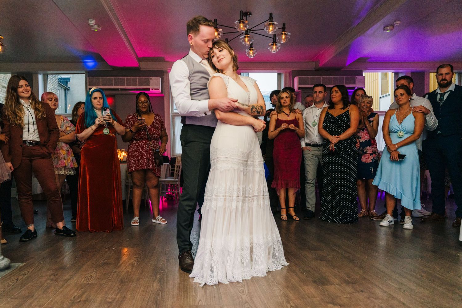 Couple shares their first dance on a dimly lit dance floor surrounded by wedding guests. PHOTOGRAPHER Dublin Ireland Wedding