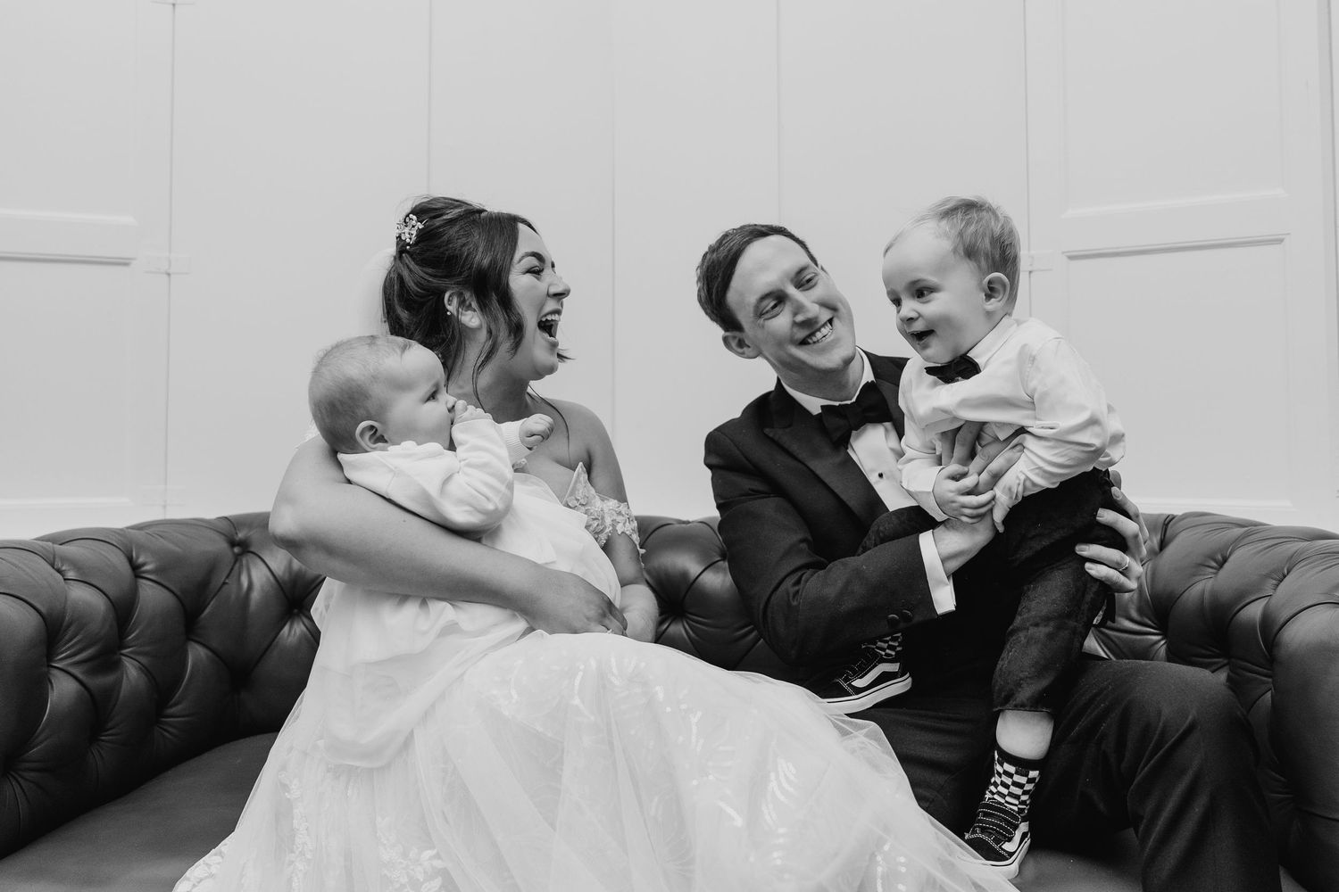 A black and white portrait of newlyweds sitting on a leather couch with two young children. Wedding PHOTOGRAPHER Dublin
