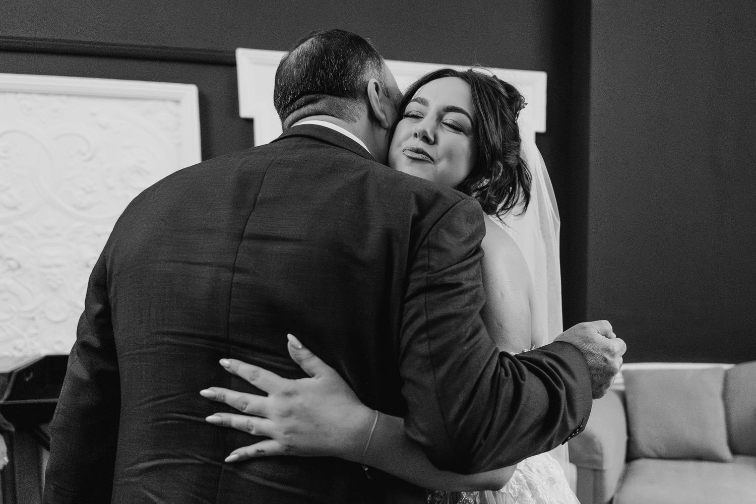 A tender black and white photograph captures an emotional embrace between a bride and person in formal attire at a wedding.  Wedding PHOTOGR