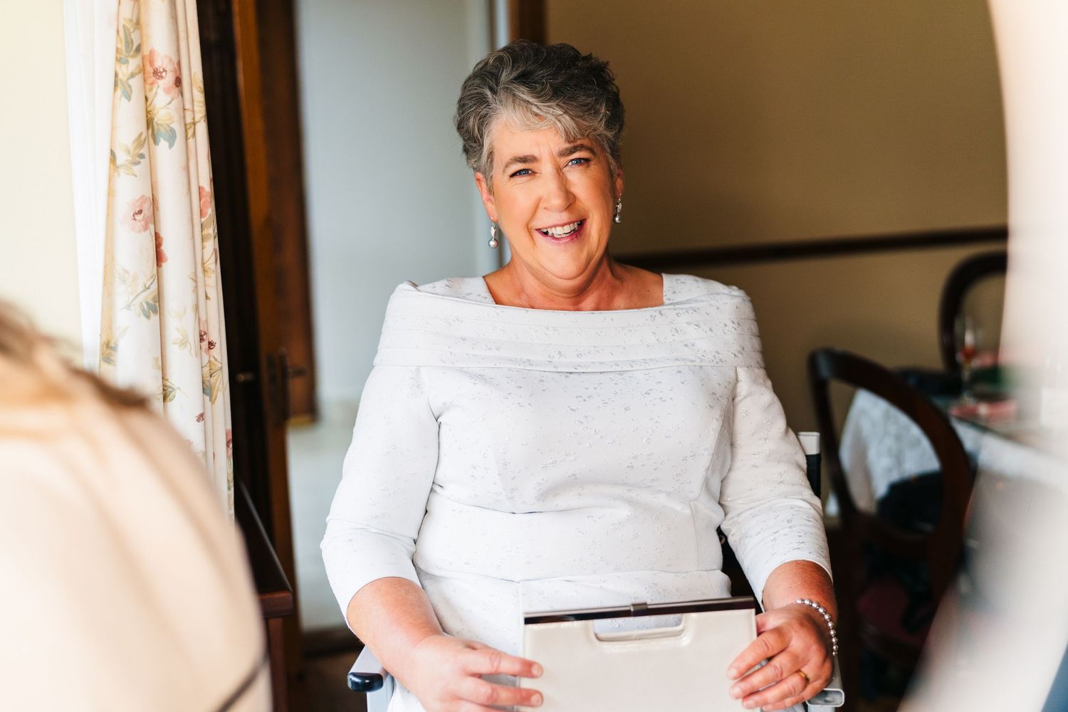 A cheerful person wearing a white blouse sits indoors near a window with natural lighting. Millhouse slane wedding photographer dublin