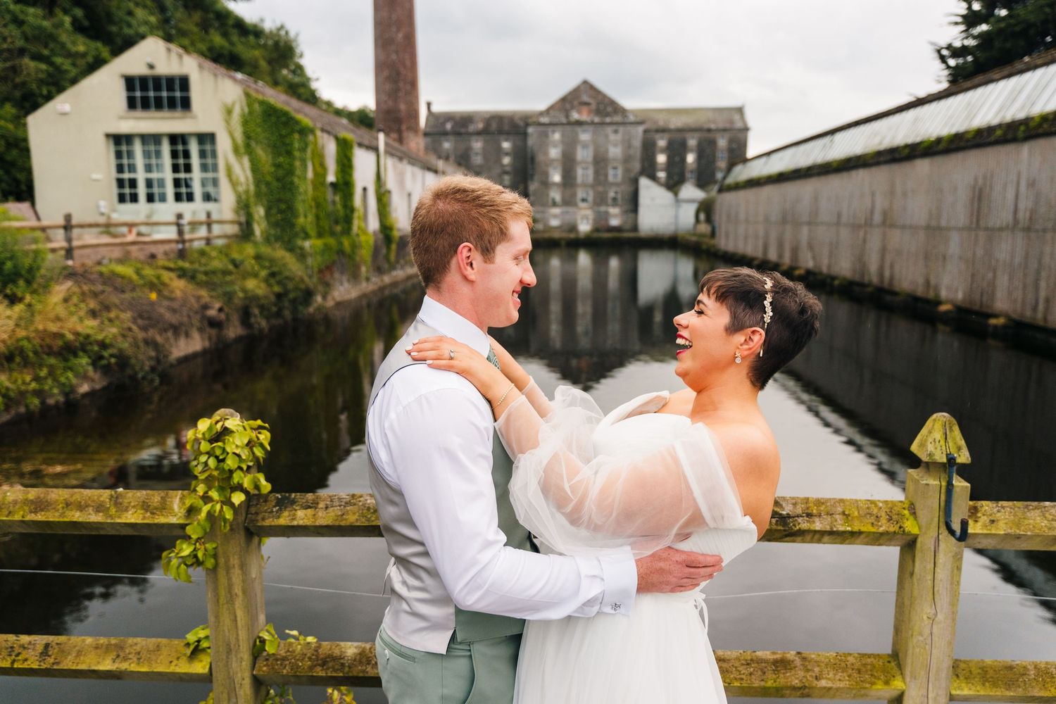 Millhouse slane wedding photographer dublin Newlyweds embrace by waterfront with industrial building and canal in background.