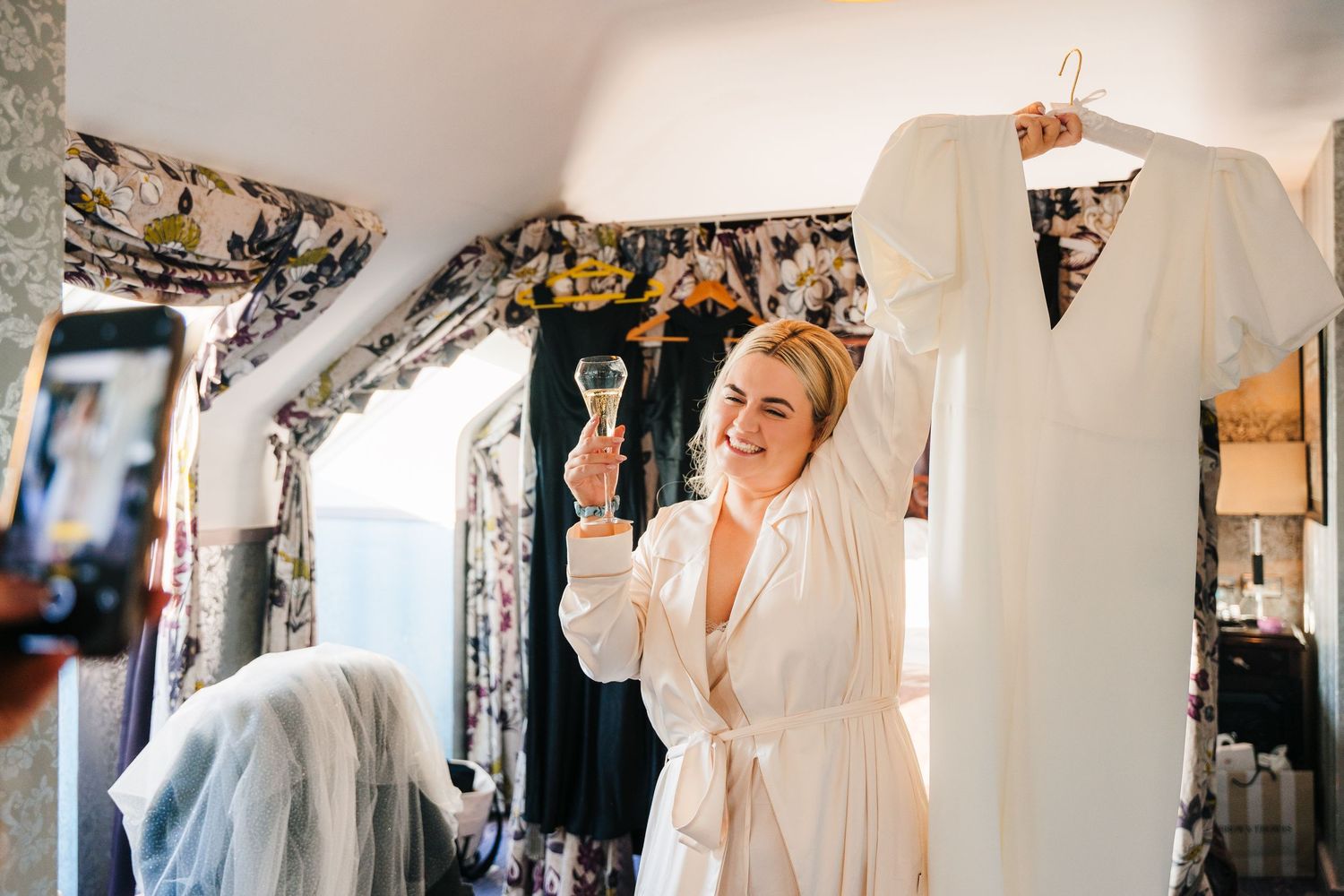 A wedding dress hangs on display while a person in a white robe gets ready by a mirror.City Hall Dublin Photographer