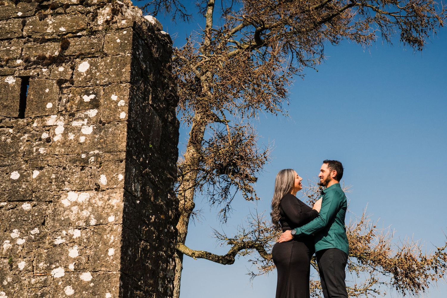 Couple sharing intimate moment by stone ruins under autumn tree branches. Family PHOTOGRAPHER Dublin