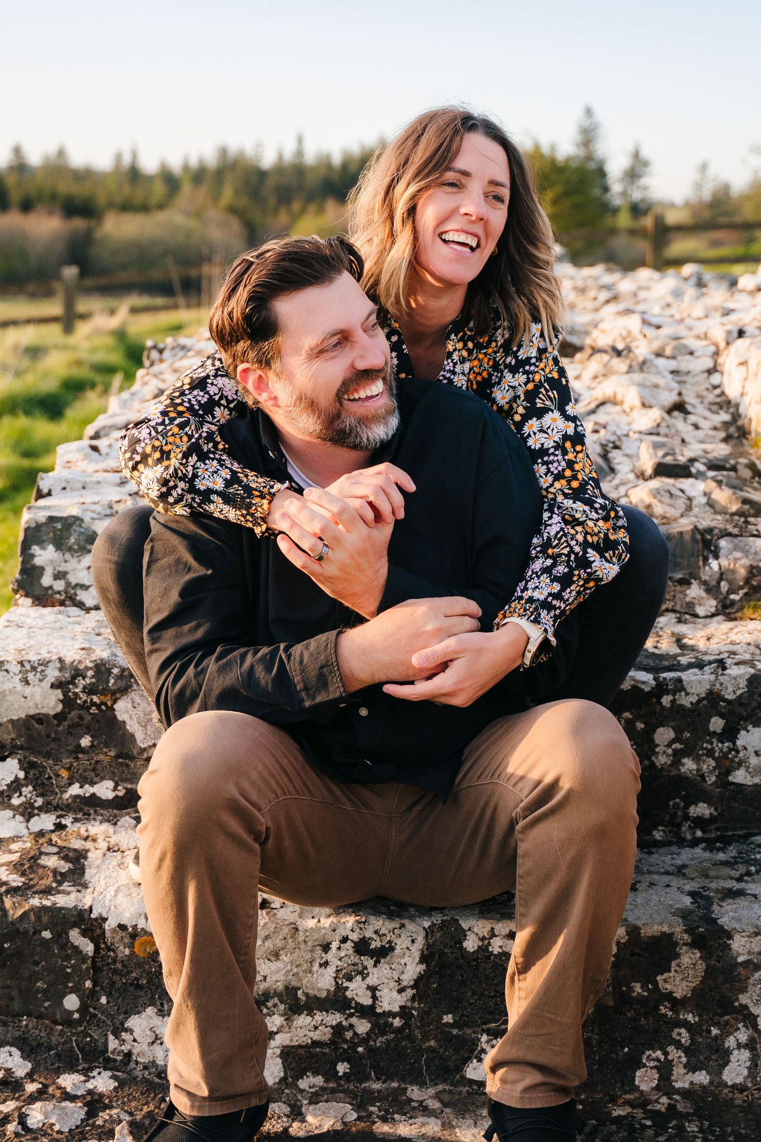 Candid laughter shared between couple sitting on ancient stone wall during sunset photo session. Photographer Ireland dublin
