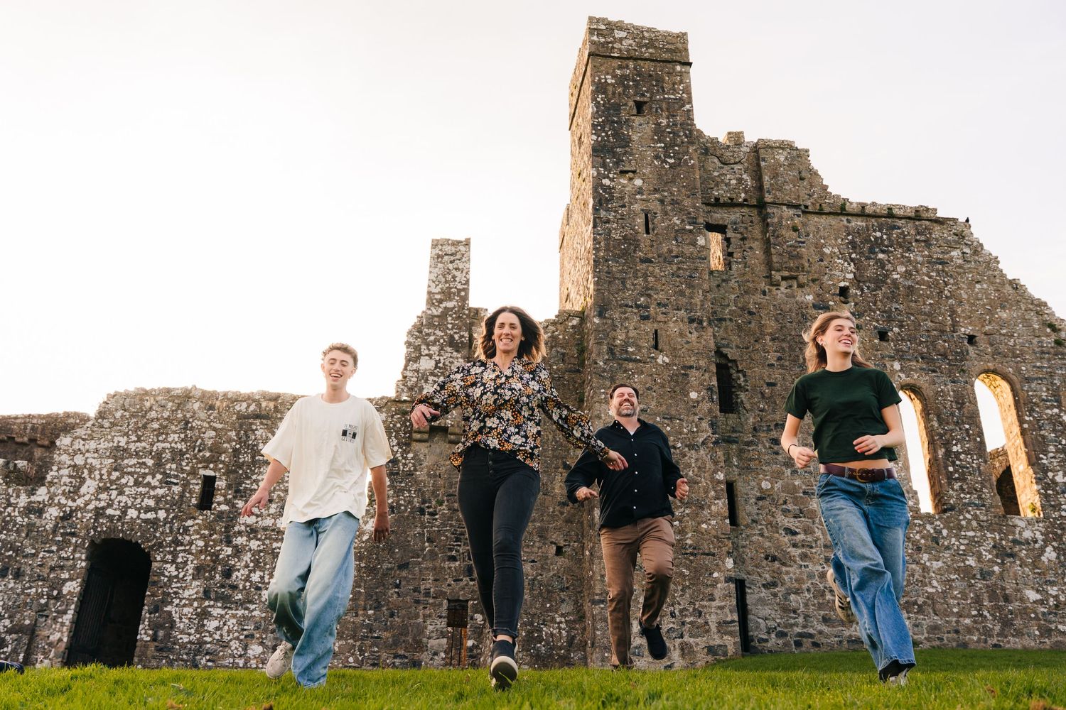 People jumping in front of an ancient stone castle ruins in Ireland against cloudy sky. Photographer Ireland dublin