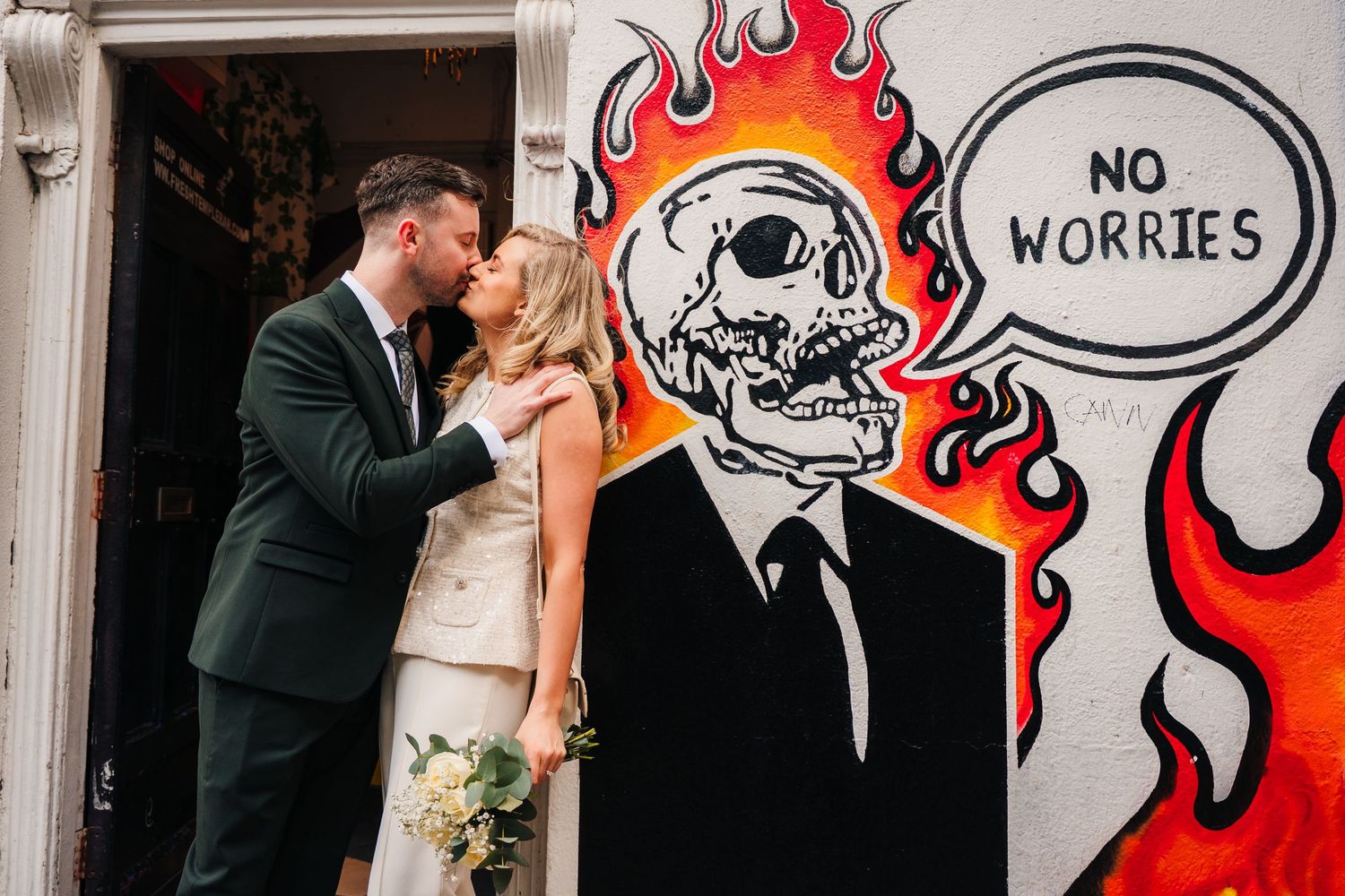 Couple poses against street art mural featuring flaming skull with 'No Worries' text.