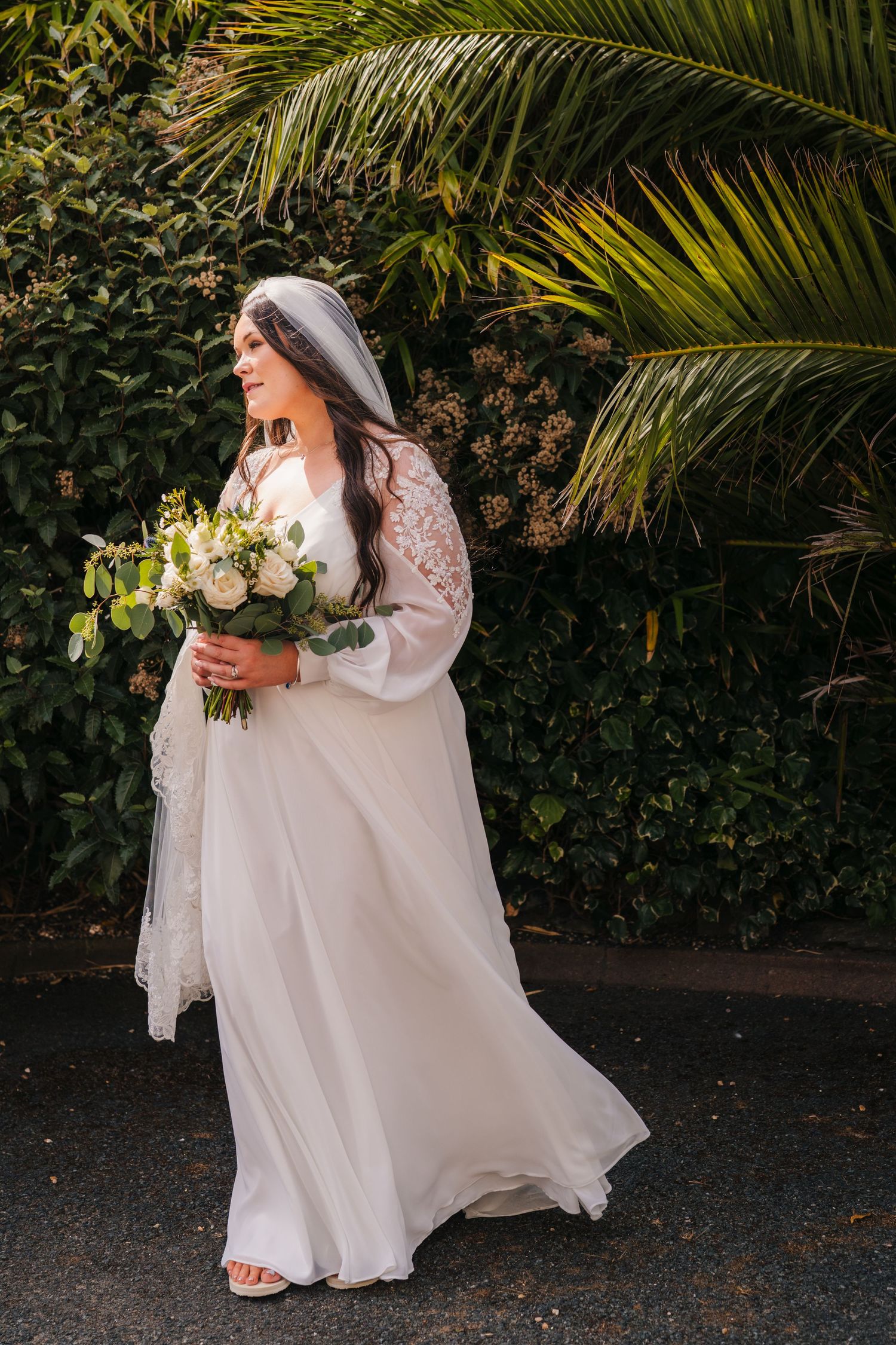 Flowing white wedding dress captured in motion against tropical palm trees and foliage. Portmarnock Hotel Wedding PHOTOGRAPHER Dublin