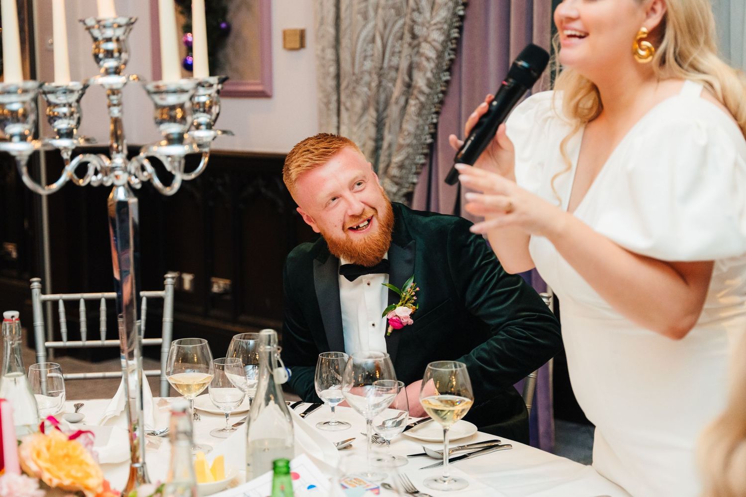 A candid reception moment captured during speeches with elegant table settings and a chandelier. Wedding photographer dublin