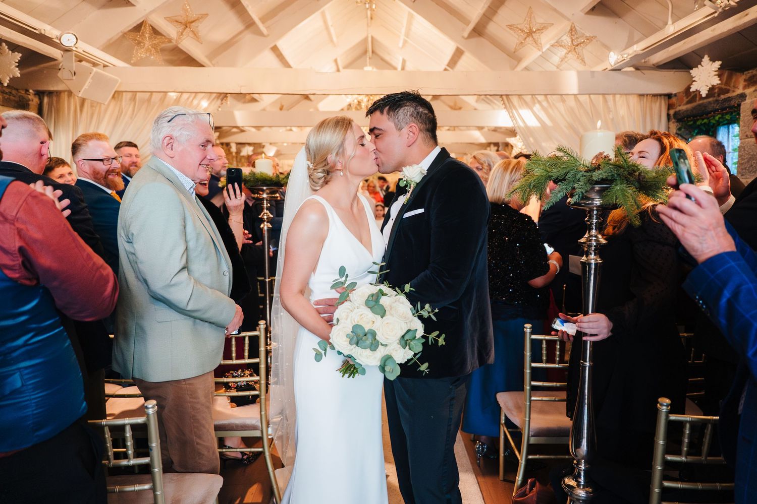 Wedding couple sharing their first kiss in a beautifully decorated indoor venue with guests watching. Ballymagarvey Wedding photographer