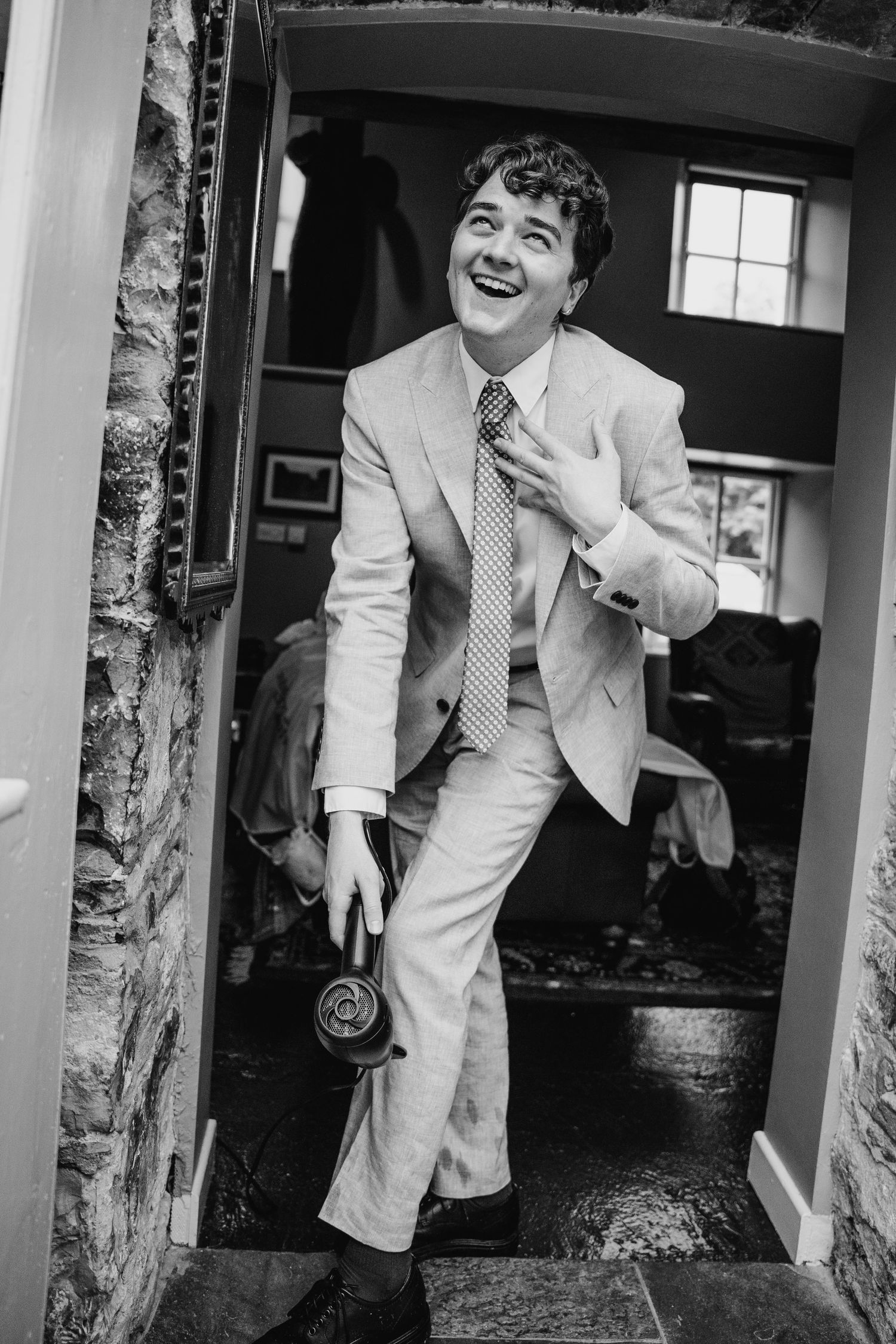 Joyful wedding party members in white suits laughing and having fun in a rustic hallway. Wedding photographer Dublin