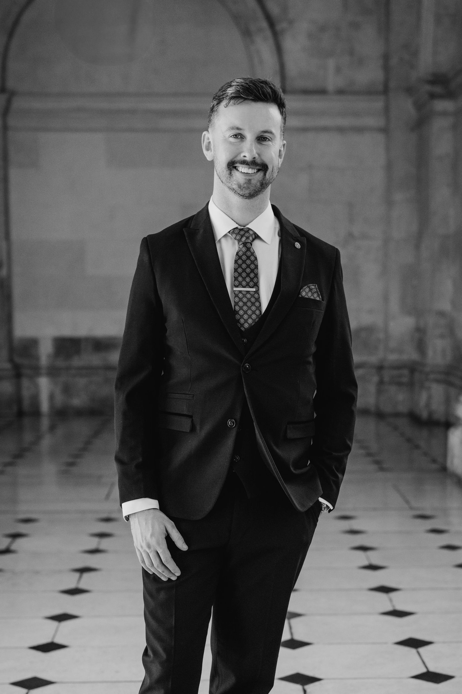 Men in formal black suits standing on checkered floor in historic building interior. City Hall Dublin wedding photogrAPher