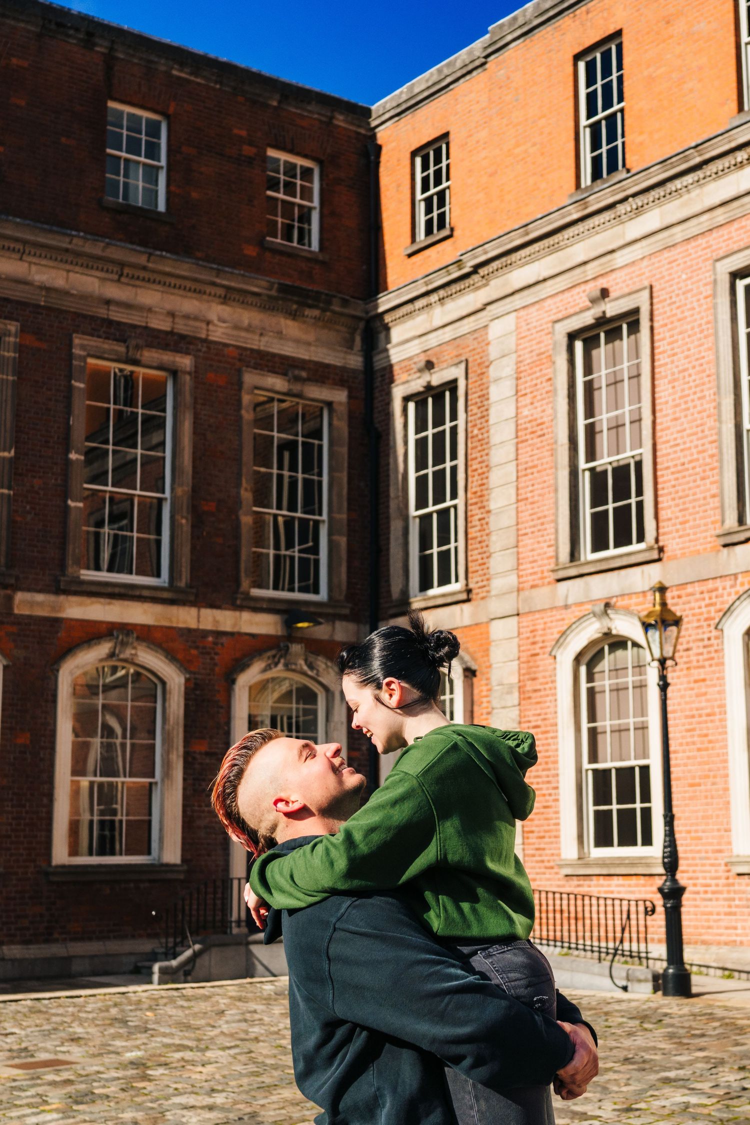 A couple embraces in a romantic pose against the backdrop of a historic orange brick building. PHOTOGRAPHER Dublin Ireland