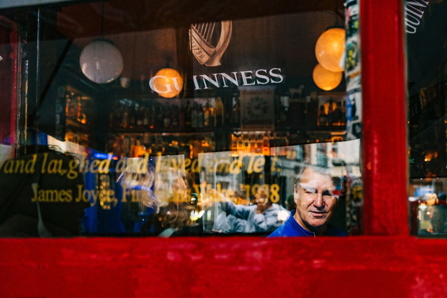Illuminated Guinness pub window display at night with red frame and glowing lanterns in background. Proposal Dublin Photographer PHOTOGRAPHE
