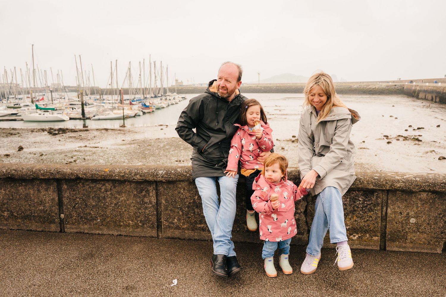 A couple sits on a seaside wall overlooking a marina filled with sailboats on an overcast day. PHOTOGRAPHER Dublin