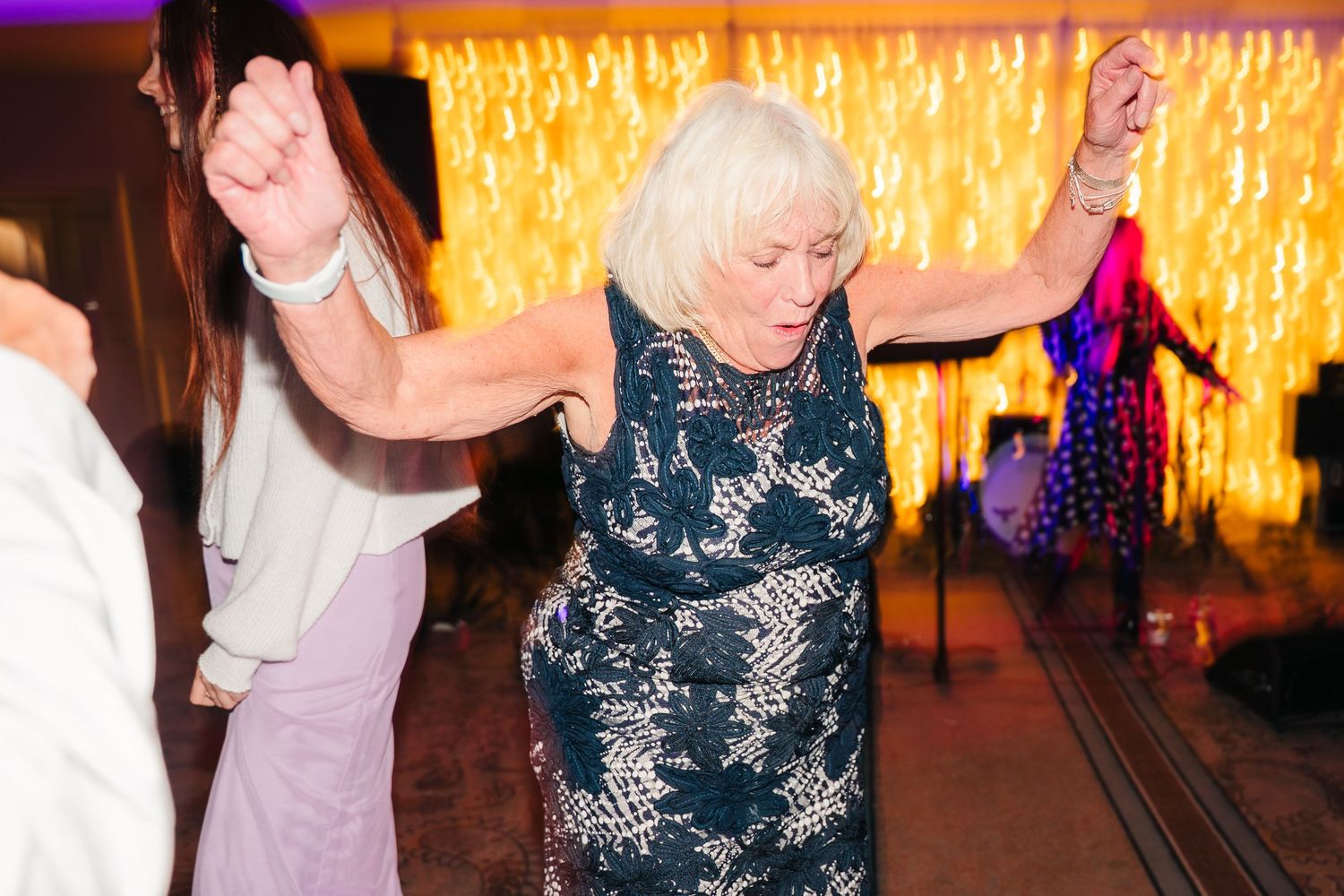 People dancing together at a wedding reception with warm glowing lights and decorations in the background. Wedding PHOTOGRAPHER Dublin