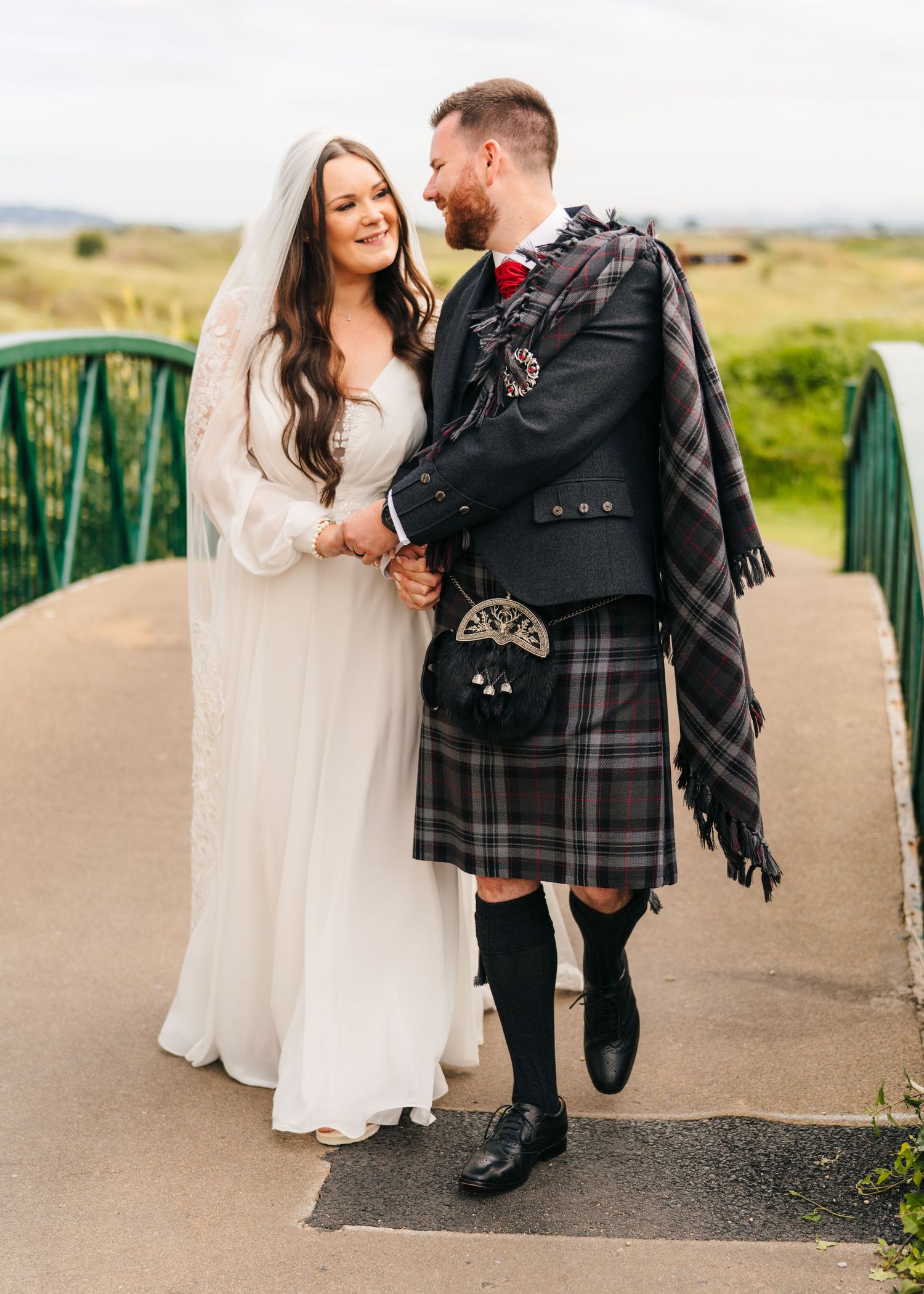 A couple share a joyful moment on a bridge, with the groom in traditional Scottish wedding attire. Portmarnock Hotel Wedding PHOTOGRAPHER Du