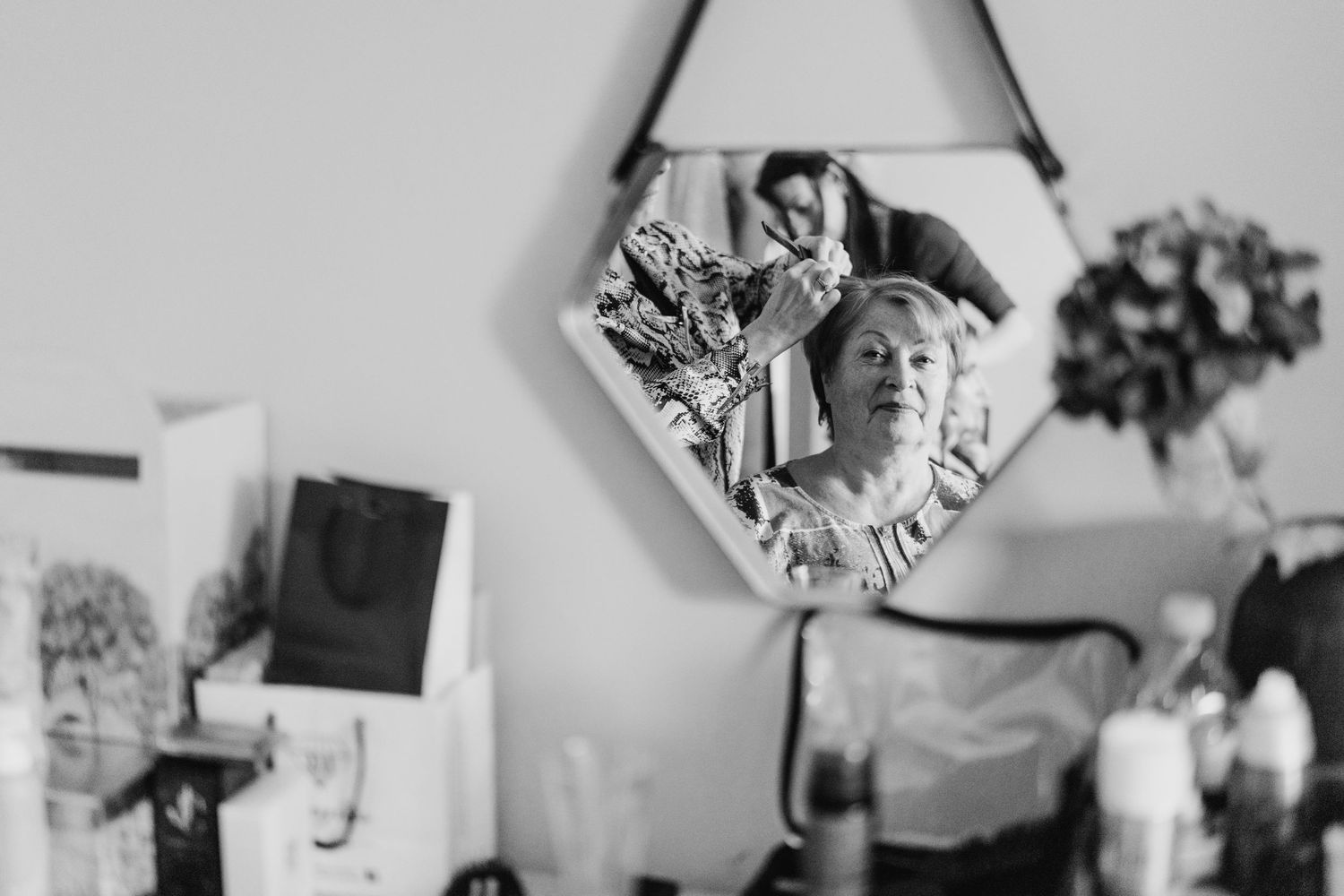 Black and white reflection in a triangular mirror showing a person getting ready while other decorative items hang on the wall. House Dublin