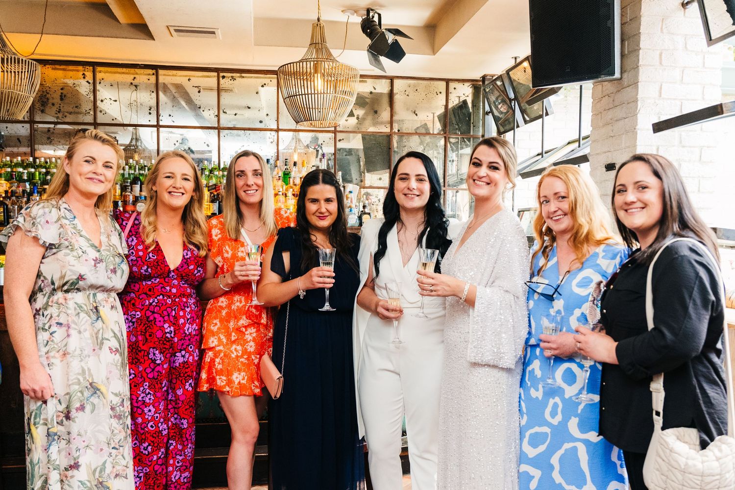 Group of friends in colorful dresses enjoying drinks and conversation at an indoor celebration event. House Dublin Wedding Photographer