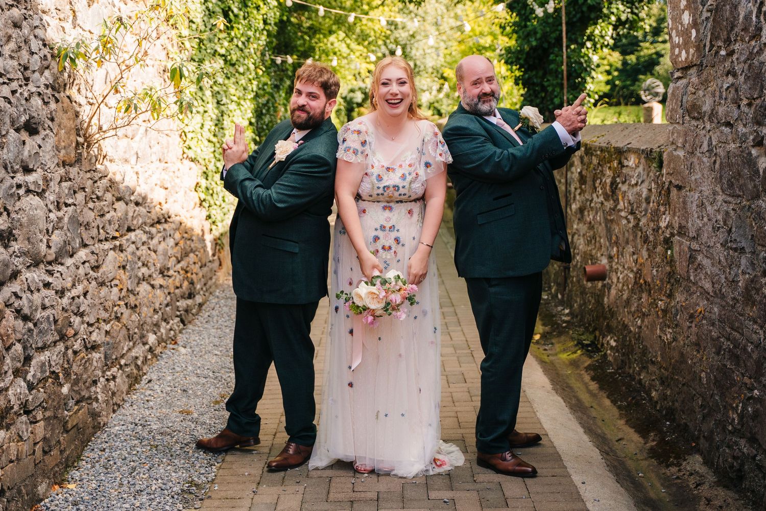 A wedding party poses playfully in a stone alleyway with the couple in the center. . Village Barn Tyrrellspass wedding photographer Ireland
