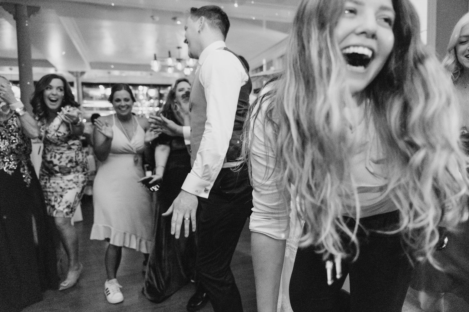 Black and white photo of joyful guests dancing and laughing together at a lively celebration party. PHOTOGRAPHER Dublin Ireland Wedding