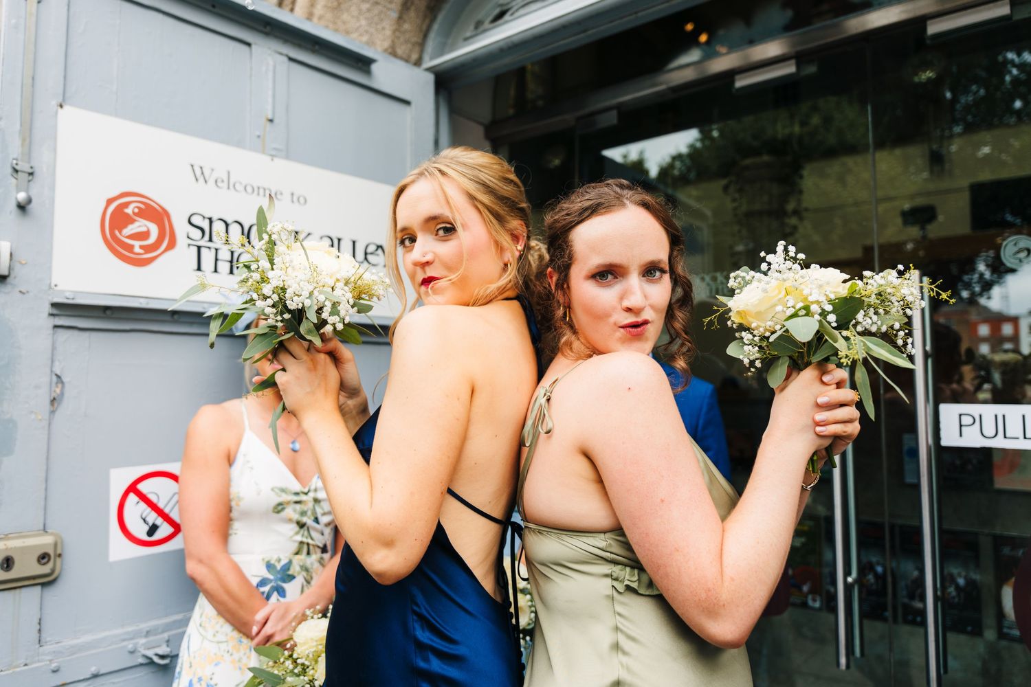Two bridesmaids in formal dresses posing back-to-back with floral bouquets. PHOTOGRAPHER Dublin Ireland Wedding