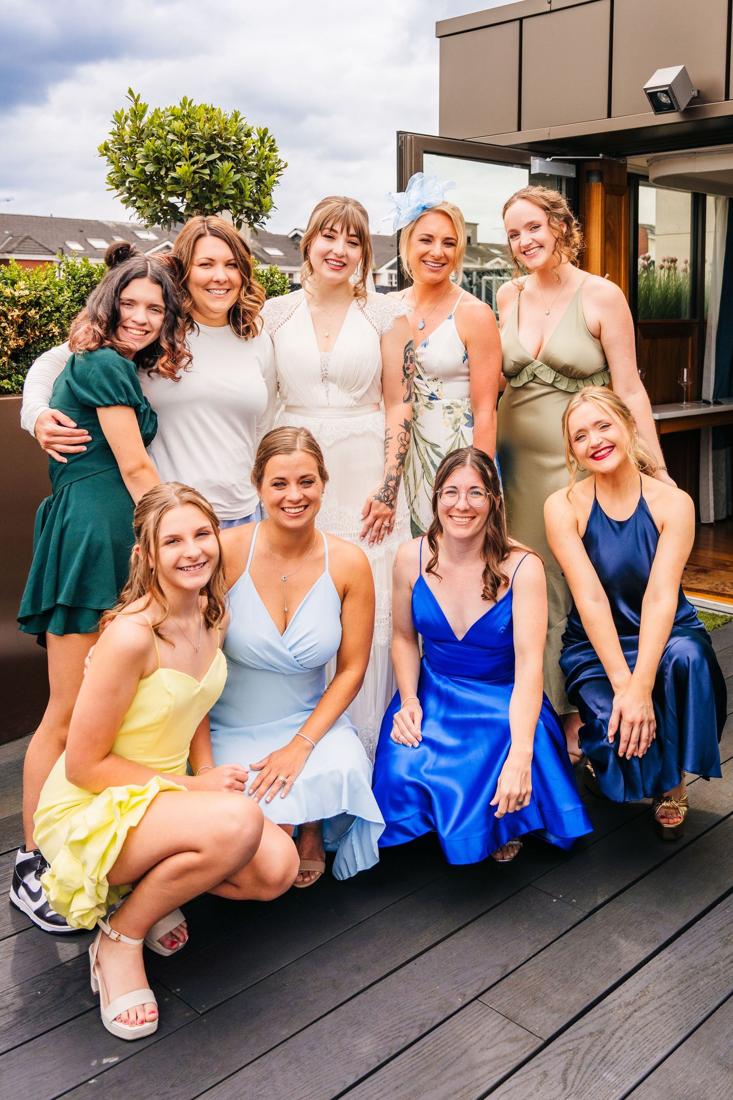 Group of wedding guests in colorful dresses pose together on an outdoor deck with mountains in background. PHOTOGRAPHER Dublin Ireland Weddi