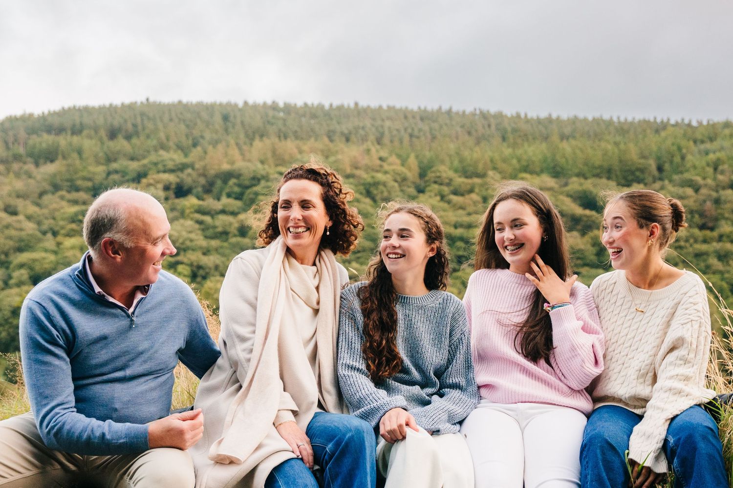 Family photographer Ireland Dublin Group of people sitting together outdoors sharing a joyful moment with mountains in the background.