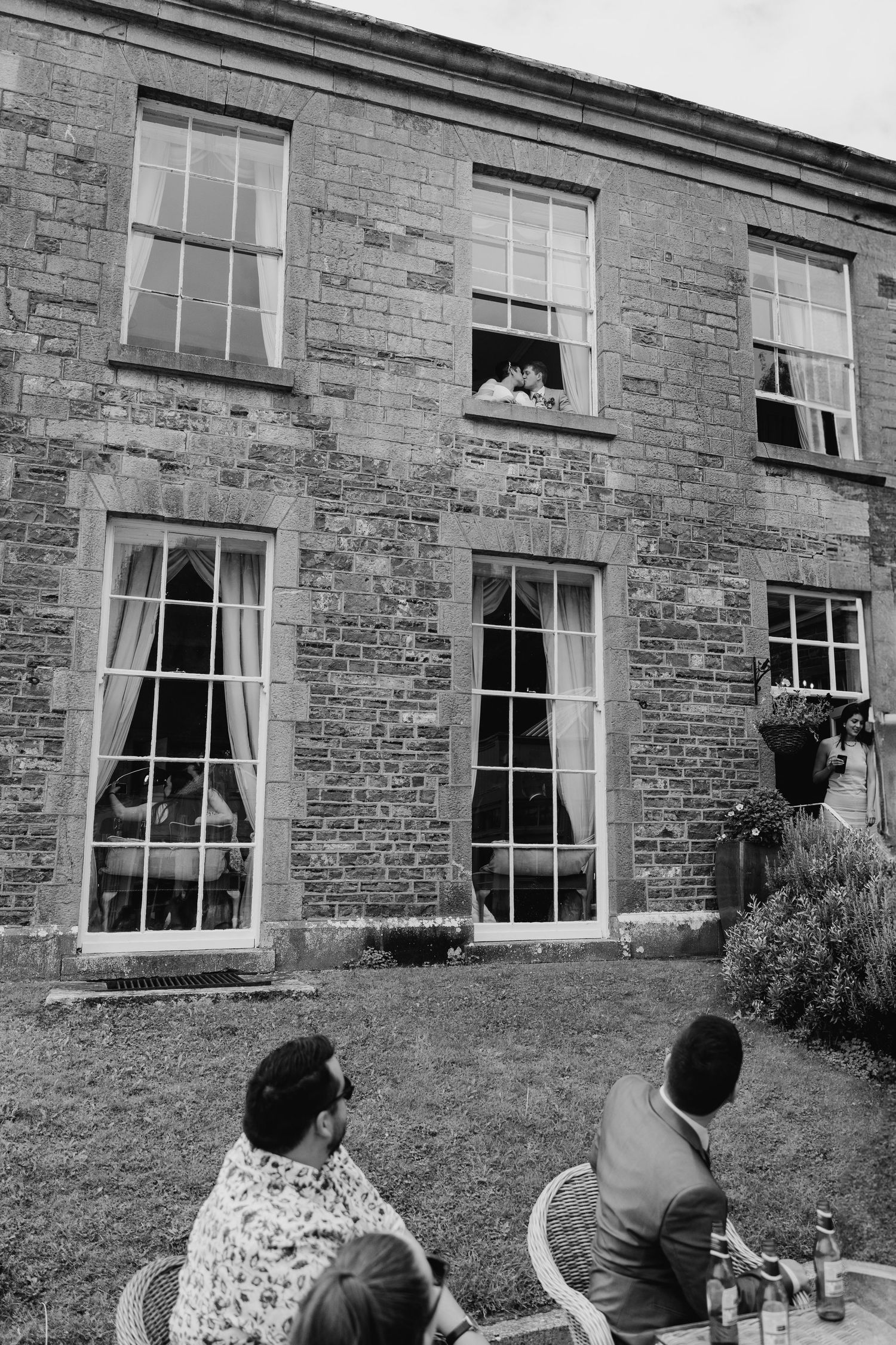Millhouse slane wedding photographer dublin Guests relax outside a stone building while watching activities through tall windows.