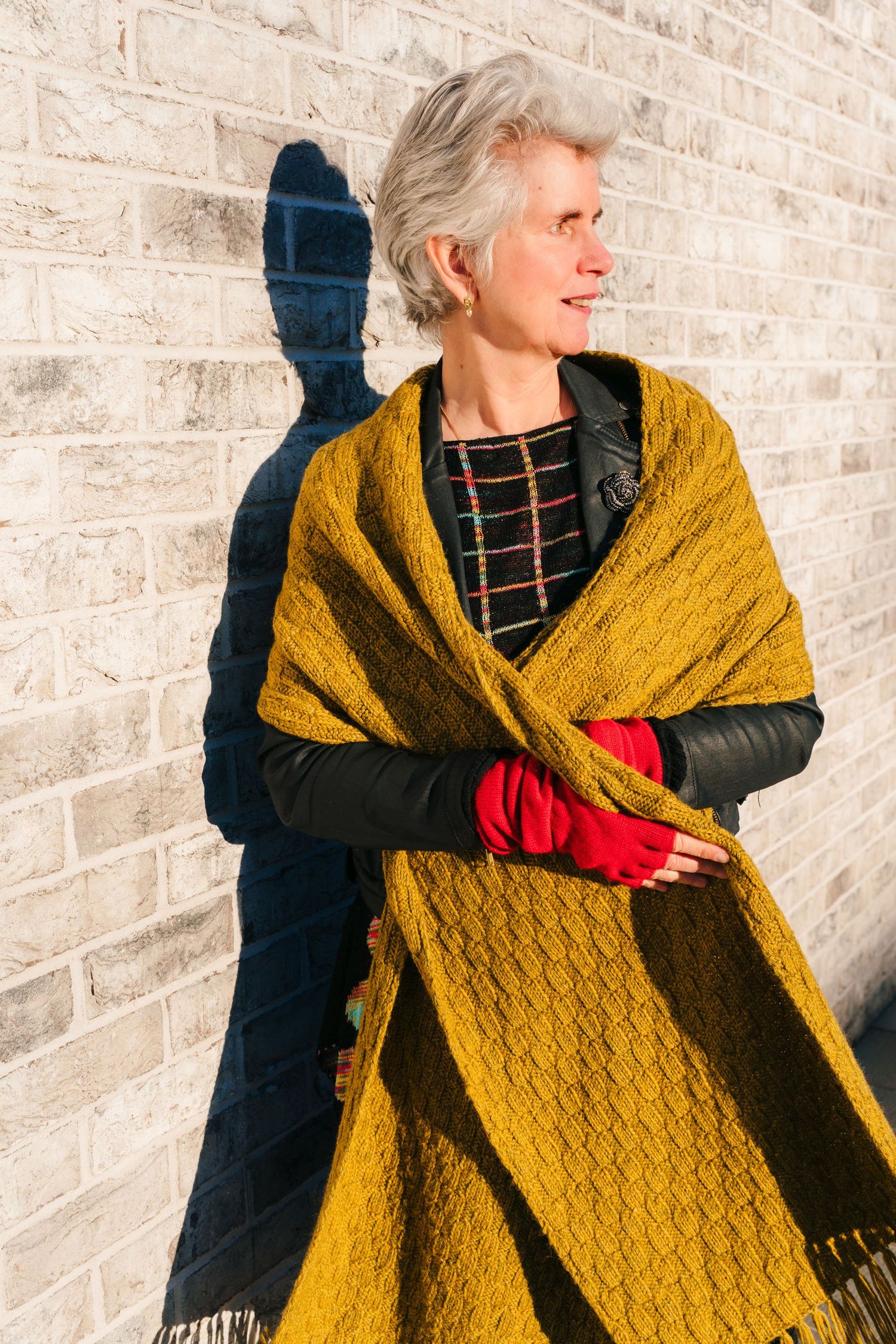 Person wearing mustard yellow knit shawl and black outfit against brick wall . Dublin professional headshots branding photographer