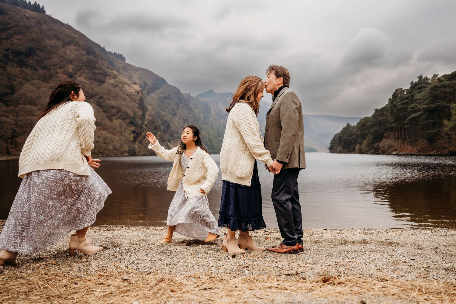 Romantic couple dances and twirls on a pebbled beach against dramatic mountain landscape and moody skies. family PHOTOGRAPHER Dublin