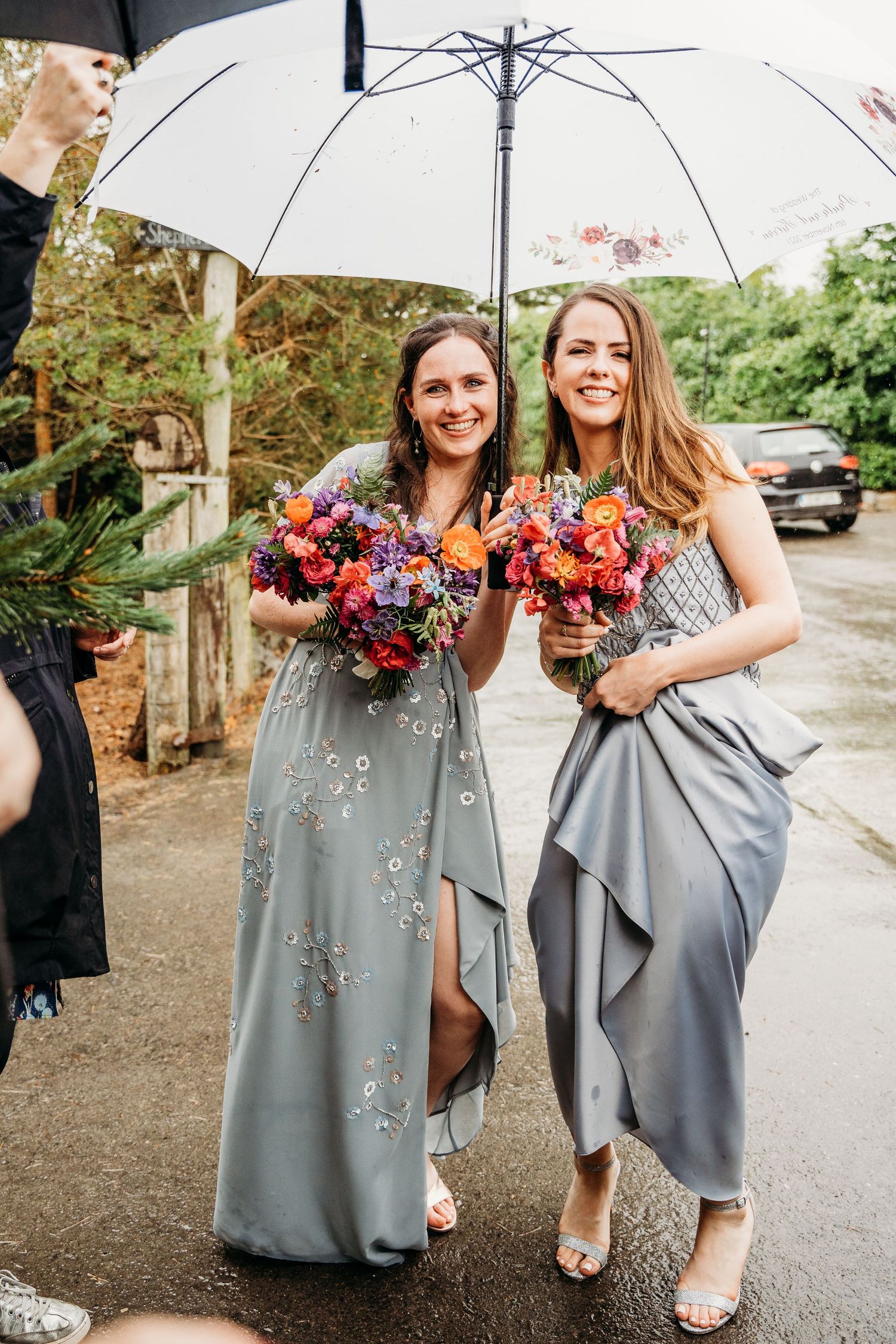 Bridesmaids in grey dresses holding colorful bouquets pose with umbrellas on a rainy day. Wedding photographer Dublin