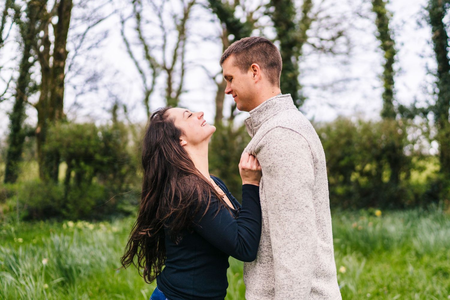 Couple embraces together in a natural outdoor setting amidst green trees and grass. PHOTOGRAPHER Dublin ireland