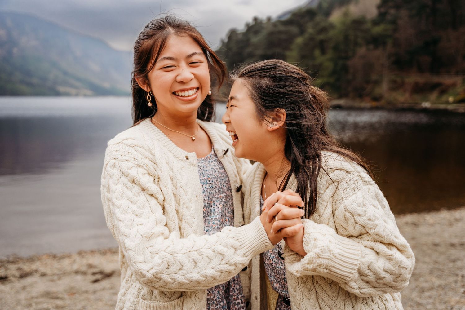 Two people sharing a joyful moment while wearing matching cream knit sweaters by a scenic mountain lake. family PHOTOGRAPHER Dublin