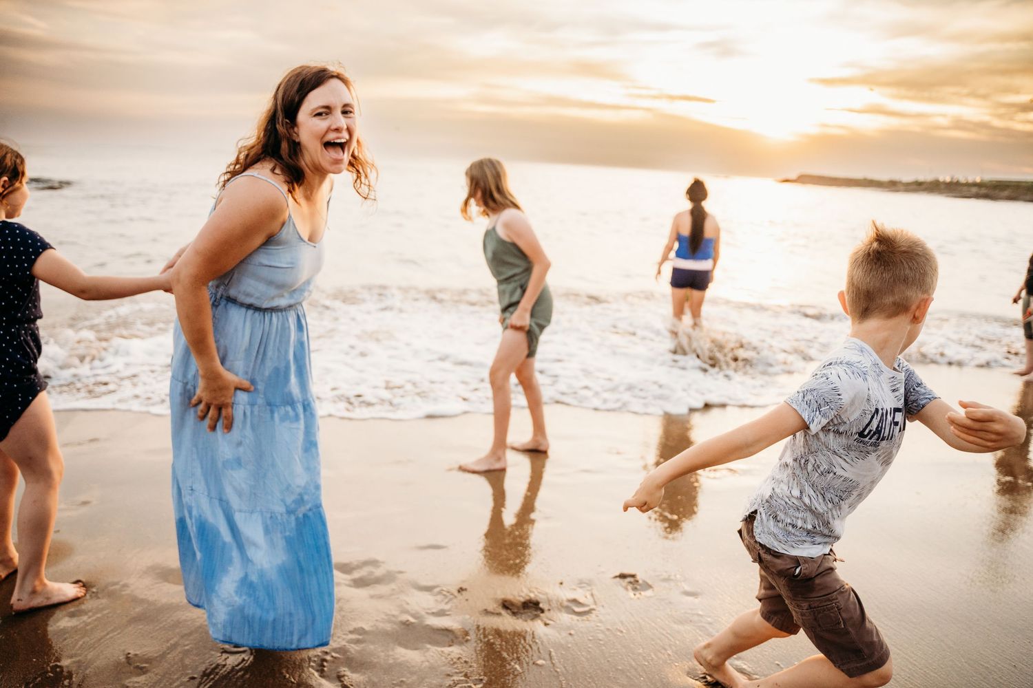 A relaxed scene of people enjoying sunset on the beach as waves lap at the shore and light glows warmly in the background. family PHOTOGRAPH