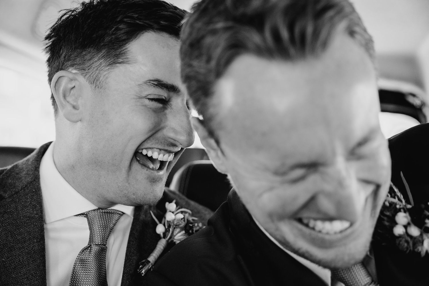 Black and white candid photo of two men in suits laughing together at a wedding celebration. Dublin wedding lgbtq photographer ireland