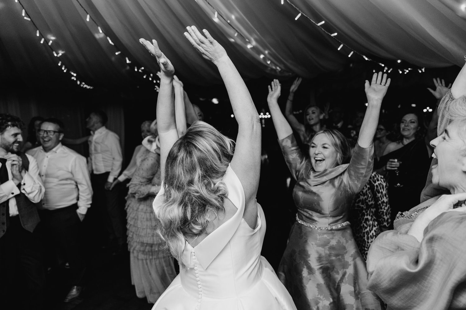 Black and white photo of wedding guests dancing and celebrating under string lights.  Virginia Park Lodge Wedding Photographer Cavan Dublin