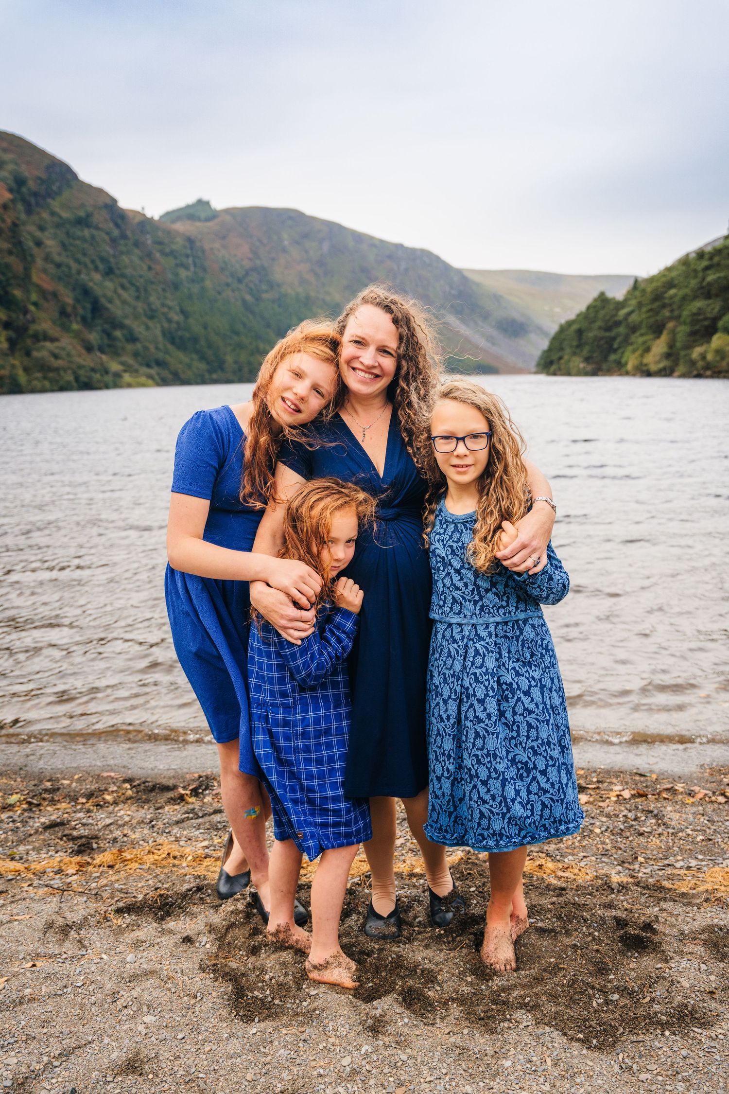 A family shares joyful moments together on a rocky beach with mountains and water in the background. Family photogrAPHER DUBLIN