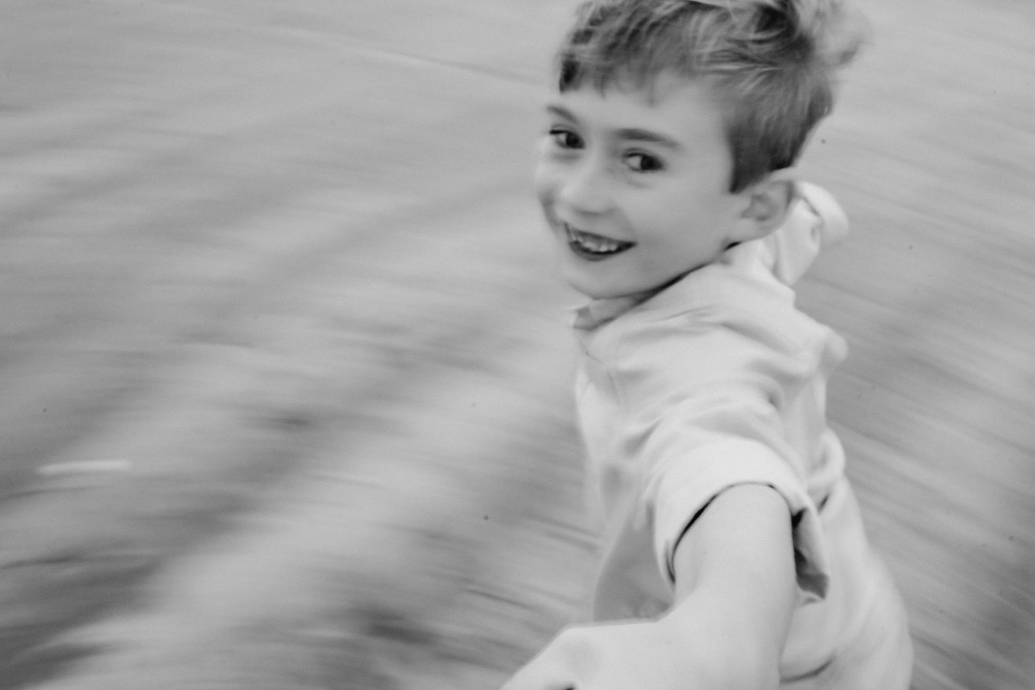 Black and white action shot of someone smiling while spinning outdoors.  Family photographer Dublin Ireland