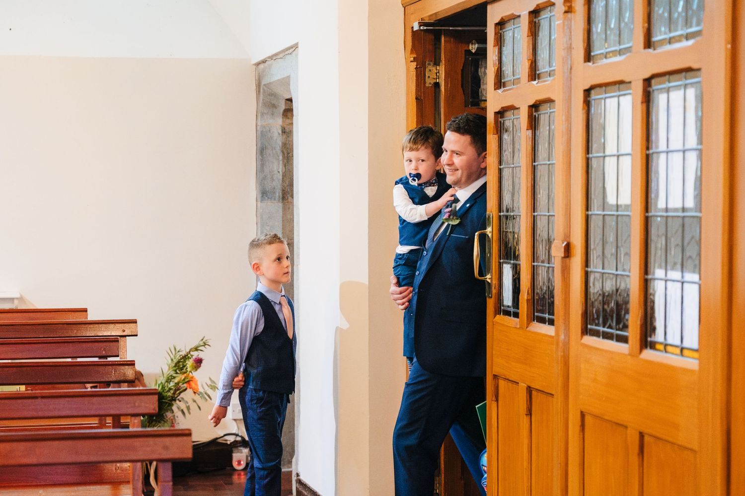 Wedding guests gathering in a church hallway with wooden doors and benches.