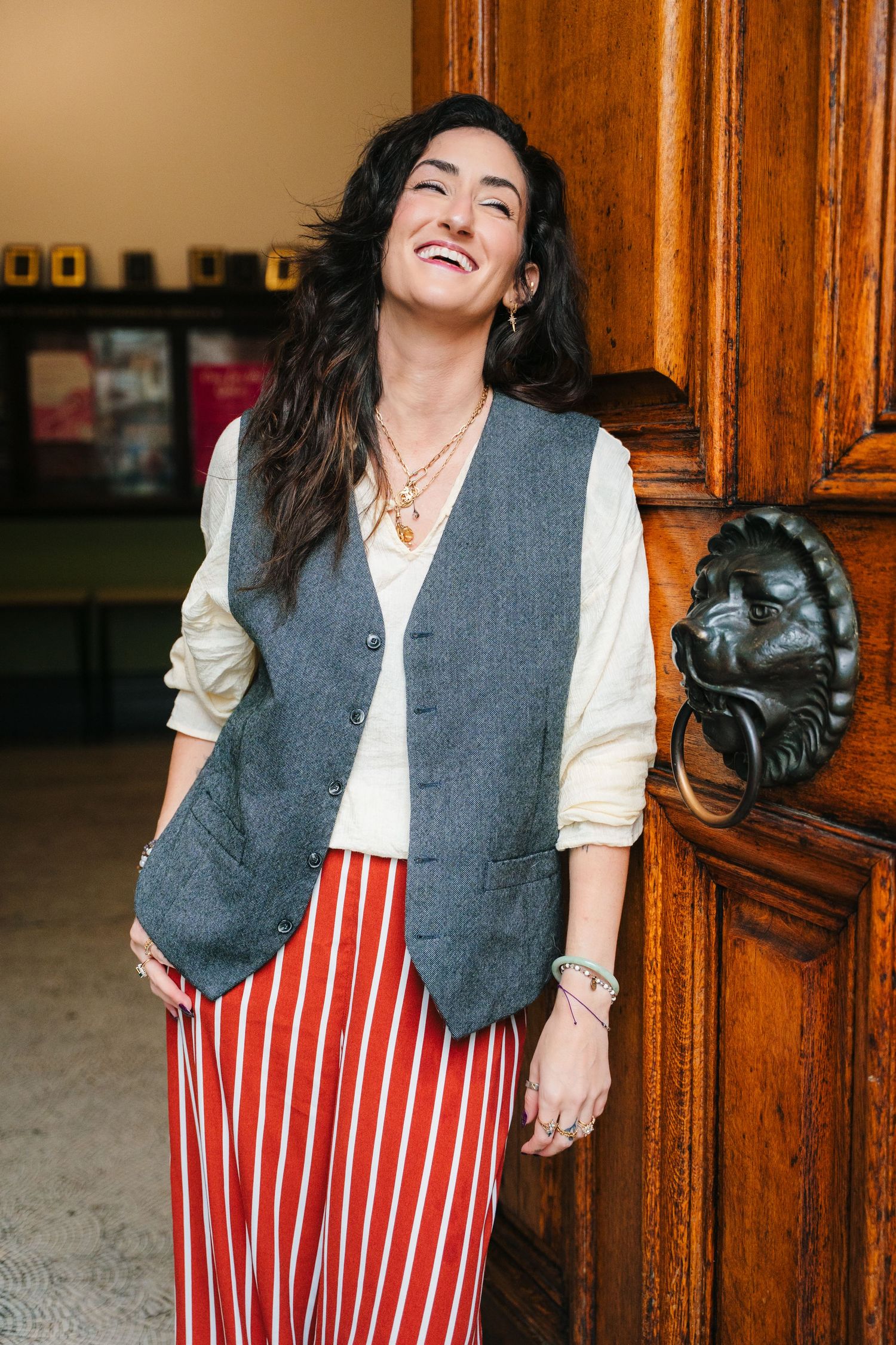 Woman wearing grey vest and white shirt laughs joyfully against wooden paneled wall. professional headshots dublin photographer