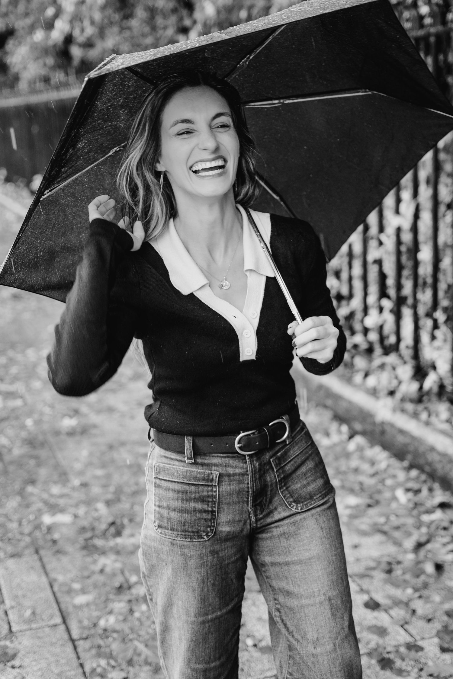 Black and white photo of someone holding an umbrella on a leaf-covered sidewalk. professional headshots dublin photographer