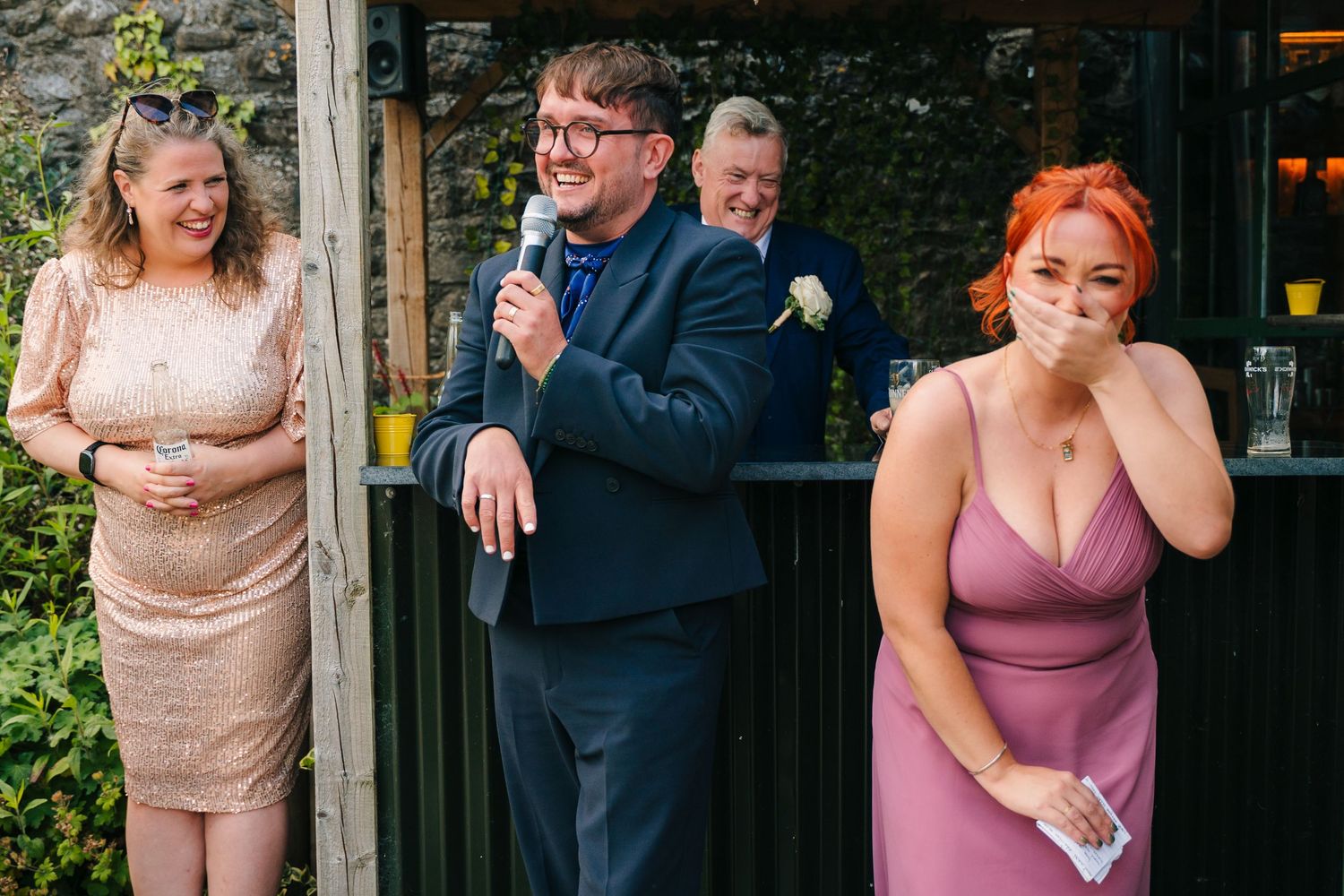 Wedding party members sharing candid laughing moments in burgundy dresses during outdoor celebration. . Village Barn Tyrrellspass wedding ph