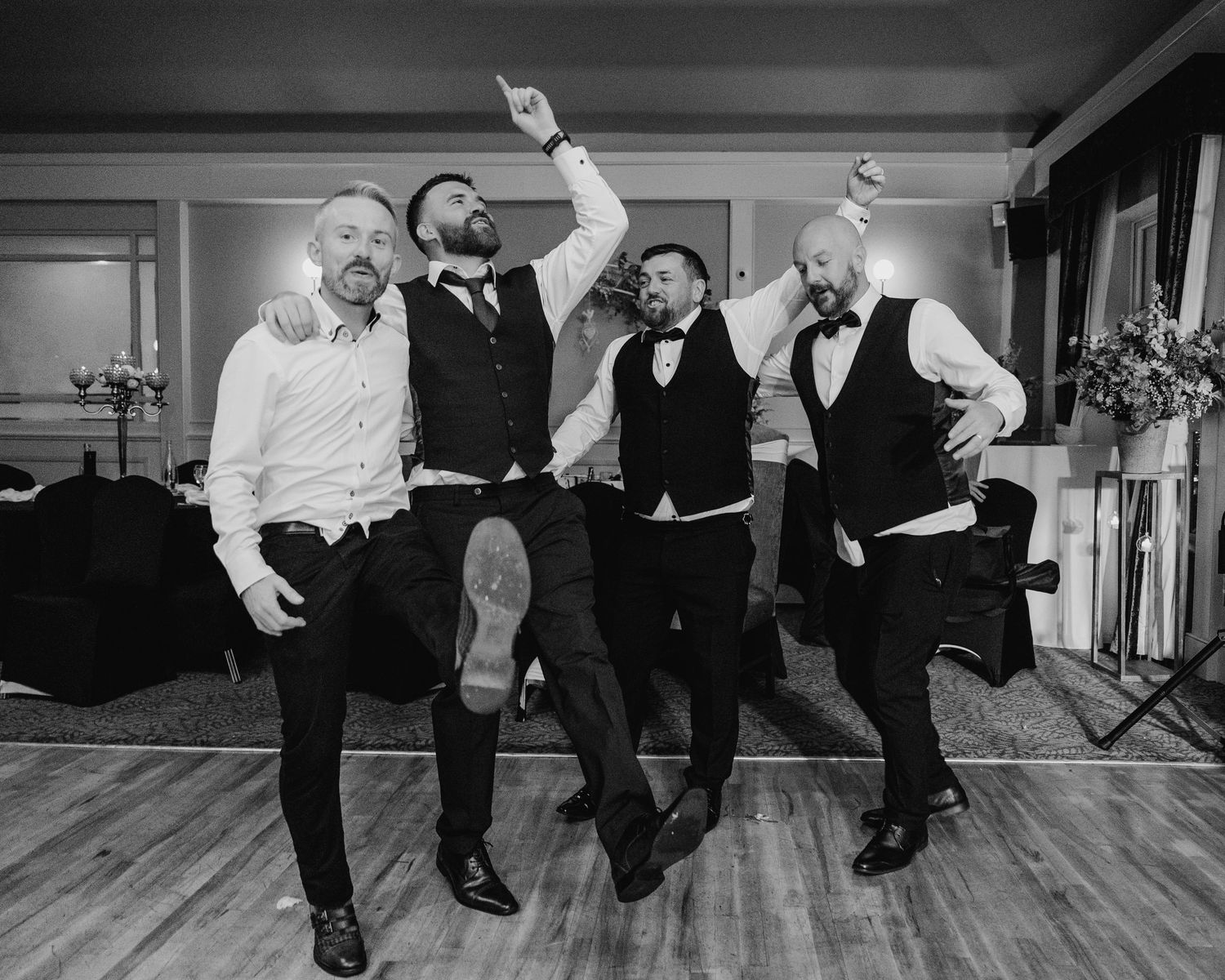 Black and white photo of four people in formal attire dancing joyfully on a wooden dance floor at an event.  photographer Dublin