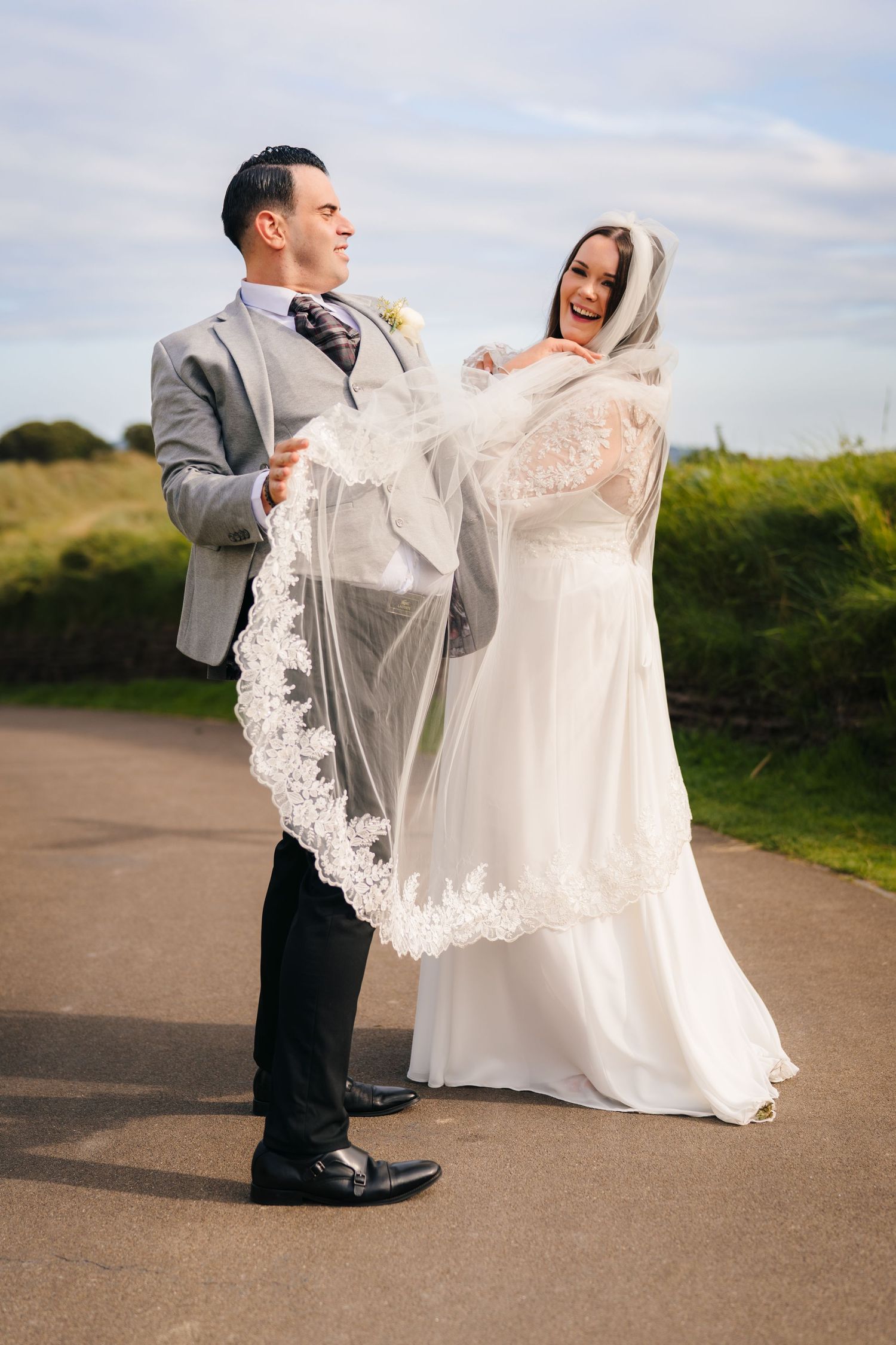 A wedding couple shares a playful moment outdoors with the bride's veil flowing in the wind. Portmarnock Hotel Wedding PHOTOGRAPHER Dublin