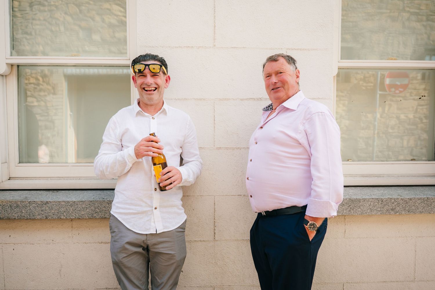 Wedding guests chat and enjoy drinks against white stone building wall. Same sex wedding PHOTOGRAPHER Dublin