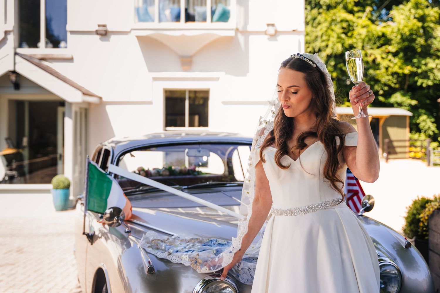 Poulaphouca Wedding photographer wicklow  Bride in white dress posing next to vintage car on sunny day.