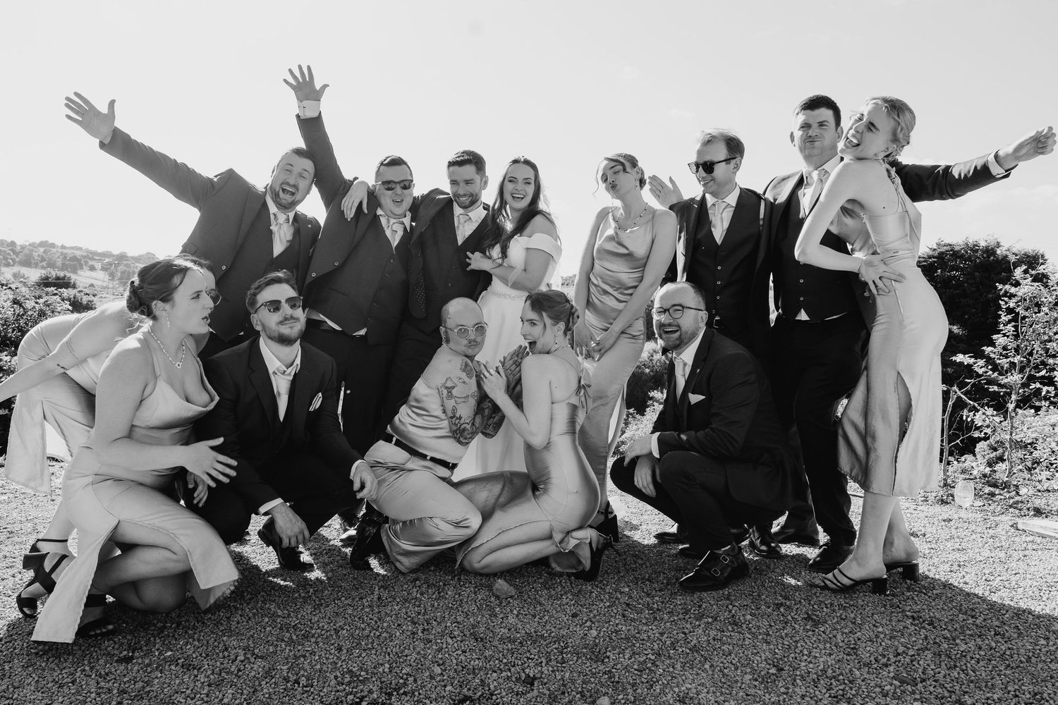 Poulaphouca Wedding photographer wicklow  Wedding party members sitting casually on grass for group photo with playful, relaxed poses.