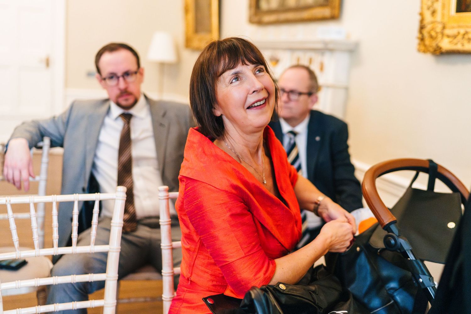 A guest in a vibrant red jacket smiles during a wedding reception.  Wedding PHOTOGRAPHER Dublin